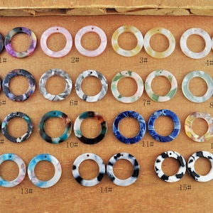 Puede incluir: Quince pares de anillos decorativos redondos de plástico de colores vivos con un agujero en el centro. Los anillos están dispuestos en filas de dos, numerados del 1 al 15.