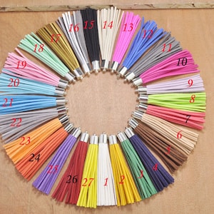 May include: A set of 27 colorful suede tassels with silver metal rings. The tassels are arranged in a circle, with the numbers 1 through 27 printed on the bottom of each tassel.