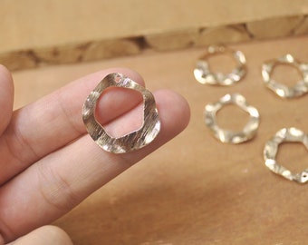 May include: Close-up of gold-colored, textured metal jewelry components. The main piece is a wavy square shape with a hole at the top. Several similar pieces are scattered in the background, suggesting a crafting or jewelry-making theme.