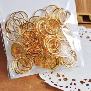 May include: A large quantity of gold-colored metal jump rings in a clear plastic bag. The rings are all the same size and are arranged in a random pattern.