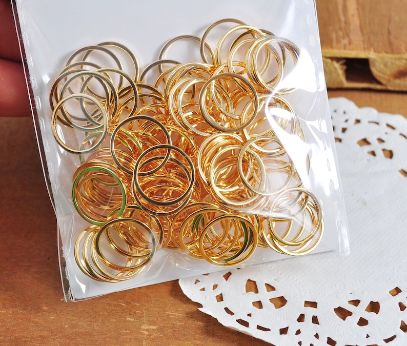 May include: A large quantity of gold-colored metal jump rings in a clear plastic bag. The rings are all the same size and are arranged in a random pattern.