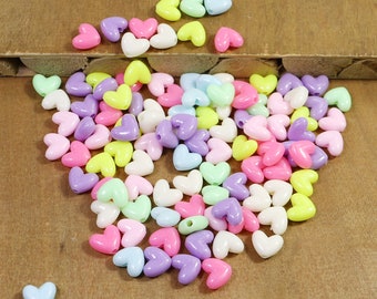 May include: A large pile of colorful plastic heart-shaped beads in shades of pink, purple, yellow, and white.