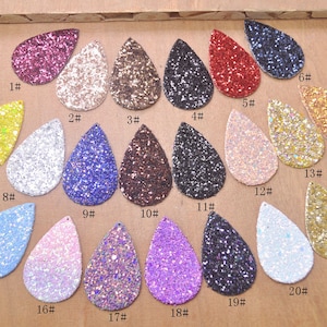 Puede incluir: Veintiún telas de purpurina de diferentes colores en forma de lágrima. La tela está dispuesta en filas y numerada del 1 al 21.