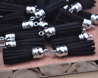 May include: A group of black suede tassels with silver metal caps. The tassels are arranged on a wooden surface.