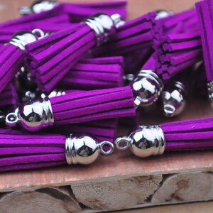 May include: A group of purple suede tassels with silver metal caps. The tassels are arranged in a pile on a wooden surface.