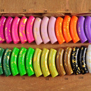 Puede incluir: Surtido de 11 cuentas de media luna con motas doradas. Las cuentas son de varios colores, incluyendo rosa, morado, naranja, verde, marrón, negro y blanco.