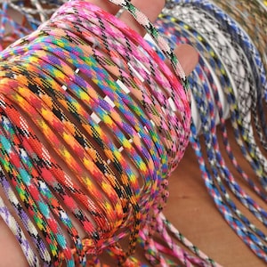 May include: A collection of colorful paracord ropes in various patterns and hues, including pink, orange, blue, and rainbow. The ropes are tightly woven and appear durable, suitable for crafting or outdoor use.