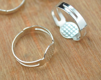 May include: Three silver ring blanks with a flat circular area for attaching a cabochon or other embellishment. The ring blanks are open on one side and have a smooth, polished finish.