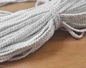 May include: A close-up of a white braided cord, showing the texture and detail of the braided pattern.
