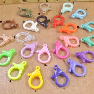 May include: Twenty-three assorted plastic lobster clasps in various colours, including green, pink, purple, blue, yellow, orange, brown, and clear.