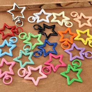 May include: A selection of star-shaped keyrings in a variety of colours, including red, blue, green, pink, orange, yellow, black, white, and purple. The keyrings are metal and have a swivel clasp.