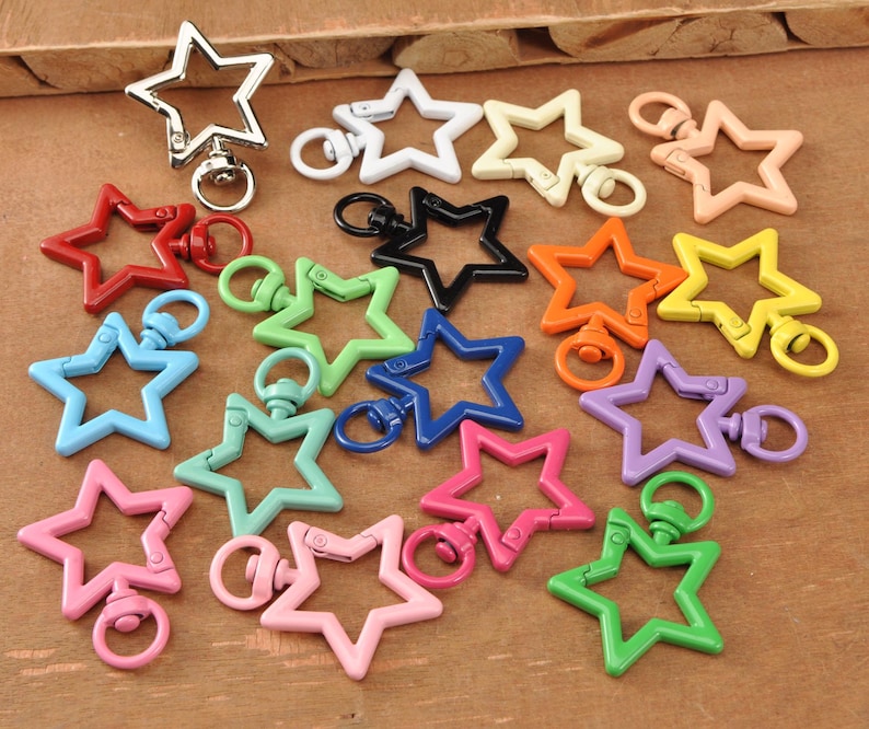 May include: A selection of star-shaped keyrings in a variety of colours, including red, blue, green, pink, orange, yellow, black, white, and purple. The keyrings are metal and have a swivel clasp.