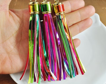 May include: Three colourful metallic tassel keychains with gold tops. The tassels are made of thin strips of iridescent material in shades of green, pink, purple, and white.
