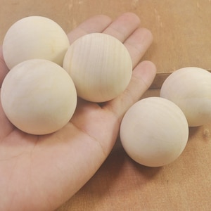 Puede incluir: Cinco bolas de madera lisas y redondas de diferentes tamaños, mostradas en una mano.
