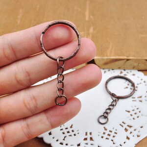 May include: Two antique copper keychains with a round ring and a short chain. The keychains are on a white doily.
