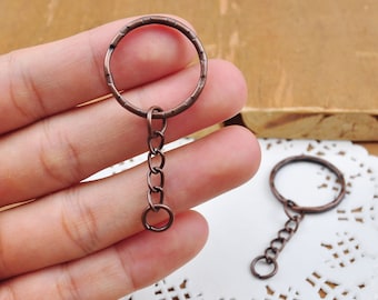 May include: Two antique copper keychains with a round ring and a short chain. The keychains are on a white doily.