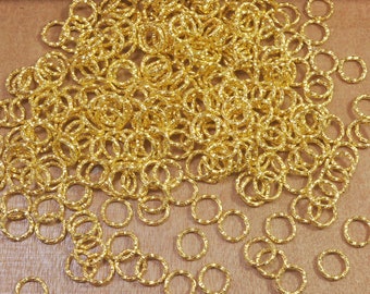 Puede incluir: Un montón grande de anillos de salto de metal de color dorado. Los anillos son todos del mismo tamaño y están dispuestos en un patrón aleatorio.