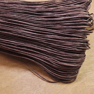 May include: A close-up of a bundle of brown waxed cotton cord. The cord is tightly wound and has a smooth, polished finish.