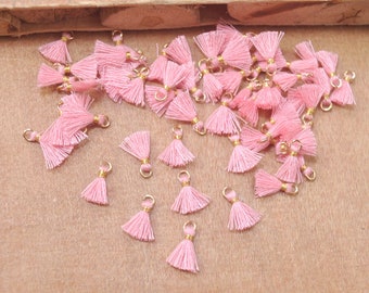 May include: A large group of pink tassel charms with gold jump rings. The tassels are made of soft, fluffy yarn and are perfect for adding a touch of whimsy to jewelry, crafts, and other projects.