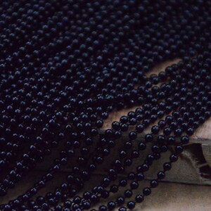 May include: A close-up of a black beaded chain. The beads are small and round, and the chain is made of many strands.