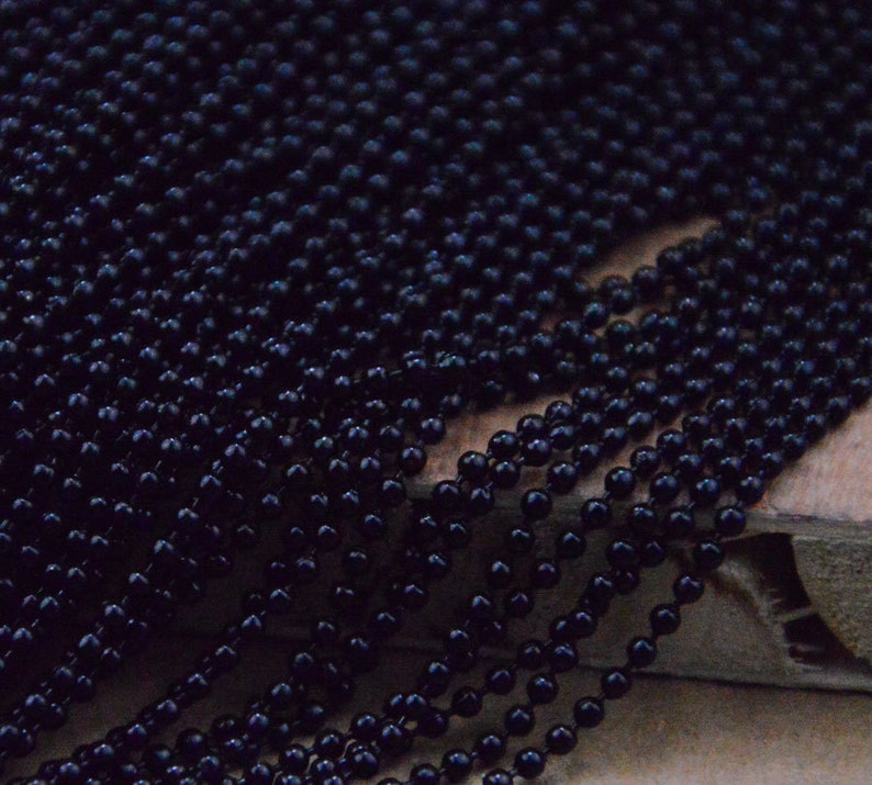 May include: A close-up of a black beaded chain. The beads are small and round, and the chain is made of many strands.