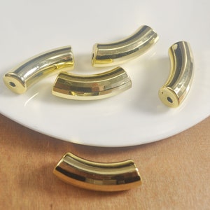 May include: Five gold-colored metal half-round beads with a ridged texture. The beads are arranged on a white surface.