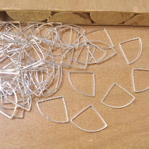 May include: A pile of silver-toned metal half-circle shapes with a textured surface. The shapes are arranged in a random pattern on a wooden surface.