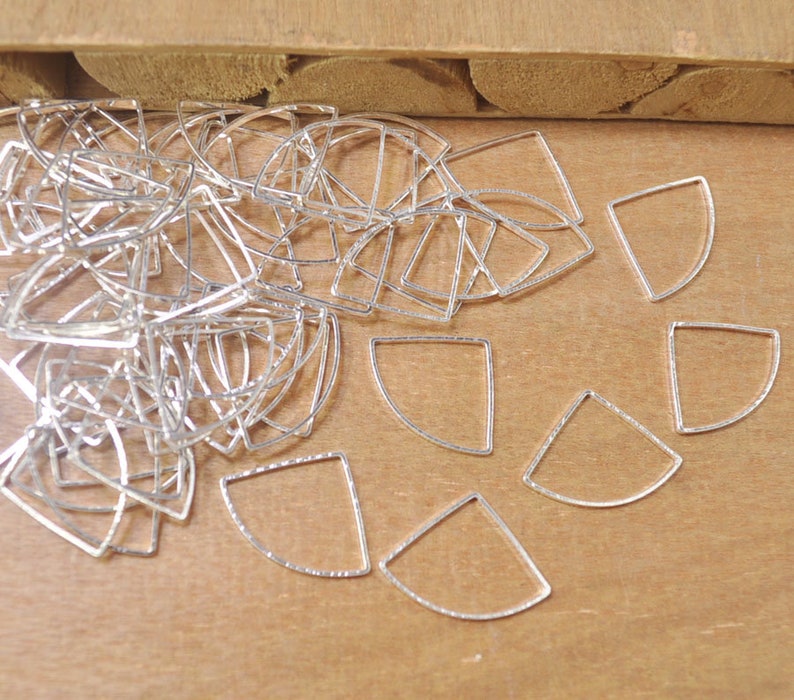 May include: A pile of silver-toned metal half-circle shapes with a textured surface. The shapes are arranged in a random pattern on a wooden surface.