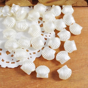 May include: A collection of white seashell-shaped beads, arranged on a white doily with a wood background.