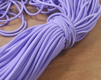 Peut inclure: Gros plan sur un paquet de cordon élastique lavande. Le cordon est doux et extensible, idéal pour les projets de bricolage.