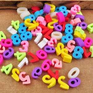 Puede incluir: Una colección de bloques de espuma con números de diferentes tamaños y colores brillantes. Los números van del 0 al 9 y son de varios colores, incluyendo rojo, azul, verde, amarillo, morado y rosa.