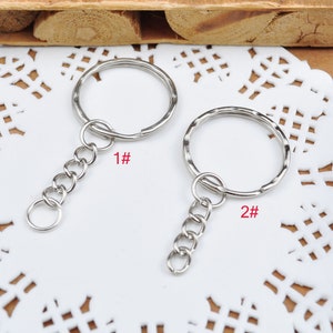 May include: Two silver keychains with a circular ring and a chain. The keychain on the left has a plain ring and the keychain on the right has a textured ring. The keychain on the left is labeled "1#" and the keychain on the right is labeled "2#"