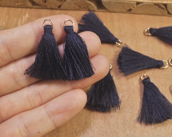 May include: A close-up of a hand holding several black tassel trim with gold rings. The tassels are made of soft, fine threads and are perfect for adding a touch of elegance to any project.
