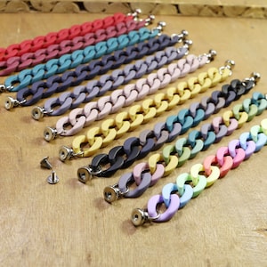 May include: A set of ten colorful chunky chain bracelets, each with a silver clasp. The bracelets are arranged in a row, with the colors ranging from red to purple.