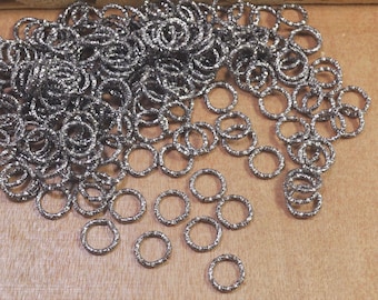 May include: A large pile of silver jump rings, some of which are scattered on a wooden surface.