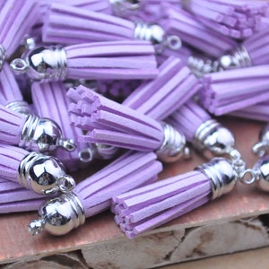 May include: A collection of lavender-coloured tassels with silver metal caps. The tassels are made of soft, fluffy material and are ideal for adding a touch of whimsy to any project.