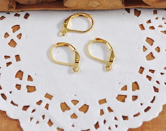 May include: Three gold-toned earring hooks, also known as ear wires, are shown on a white doily. The hooks are made of metal and have a spring-loaded closure.