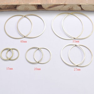 Puede incluir: Cinco juegos de aros de metal de color dorado en diferentes tamaños. Los aros están dispuestos en una fila del más pequeño al más grande. Los tamaños están etiquetados en milímetros: 15 mm, 20 mm, 27 mm, 35 mm y 40 mm.