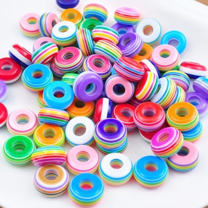Pode incluir: Uma coleção de contas de plástico listradas coloridas. As contas são redondas e têm um furo no centro. São perfeitas para fazer joias ou outros trabalhos manuais.