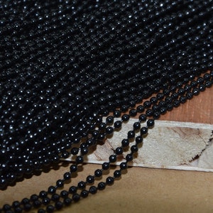 May include: A close-up of a black metal chain made of small round beads. The chain is lying on a wooden surface.