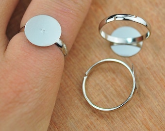 May include: Three silver ring blanks with round, flat, silver-colored bases. The bases are designed to be filled with resin, glass, or other materials.