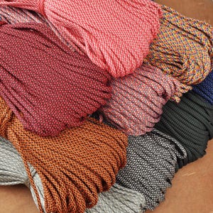 May include: A collection of colorful paracord bundles in various shades, including red, orange, gray, black, and blue. Each bundle is tightly wound, showcasing the textured pattern of the cord. The cords are arranged in a visually appealing, overlapping manner.