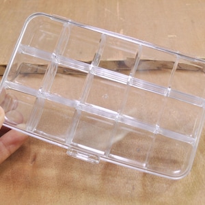 May include: A clear plastic storage box with multiple compartments. The box is empty and has a rectangular shape.
