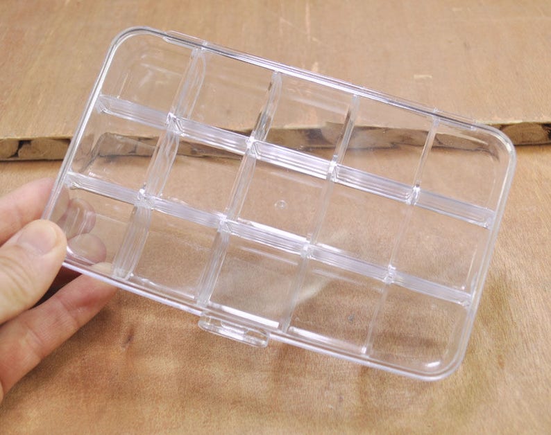 May include: A clear plastic storage box with multiple compartments. The box is empty and has a rectangular shape.