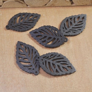 May include: Five black wooden leaves with intricate cut-out designs. The leaves are arranged in a cluster on a brown surface.