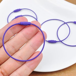 May include: Purple metal key rings with a crimped closure. The key rings are made of a thin, flexible cable.