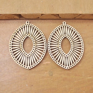 May include: Two wooden earrings with a sunburst design and a cutout oval in the center. The earrings are a light brown color and have a smooth finish.