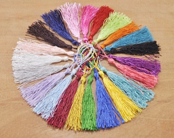 May include: A collection of colorful tassels in various shades, including pink, blue, green, red, and yellow. The tassels are arranged in a circle on a wooden surface.