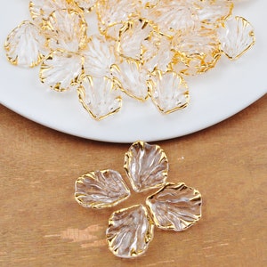 May include: A pile of clear plastic flower petals with gold trim. The petals are scattered on a white plate. A single flower made of four petals is shown on a wooden surface.