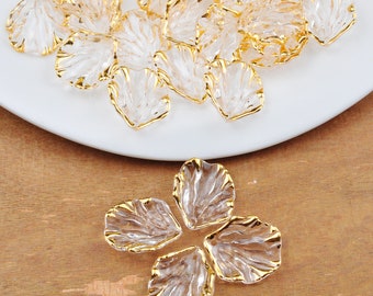 May include: A pile of clear plastic flower petals with gold trim. The petals are scattered on a white plate. A single flower made of four petals is shown on a wooden surface.